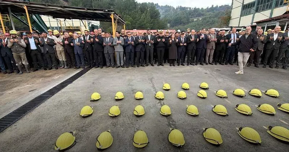 Amasra'da maden ocağı kuyusu başındaki anmada yere dizilmiş sarı baretler ve arkalarında sıra halinde duran katılımcılar