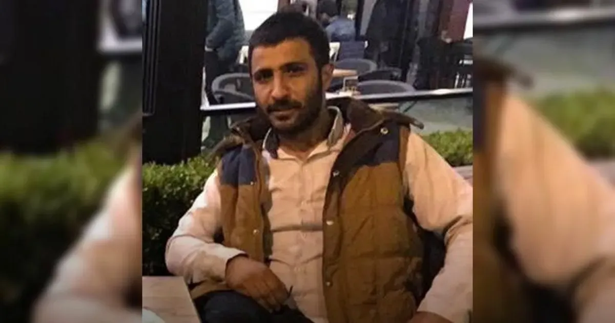 Hayatını kaybeden işçi Erkan Kundo, kahverengi yelek ve açık renk gömlekle bir kafede oturuyor; fotoğrafın iki yanı bulanık