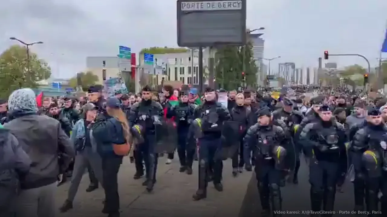 Paris Porte de Bercy’de koyu üniformalı polis hattı kalabalığın önünde aynı yönde yürüyor; arkada bayraklı göstericiler. Viral videodan kare.